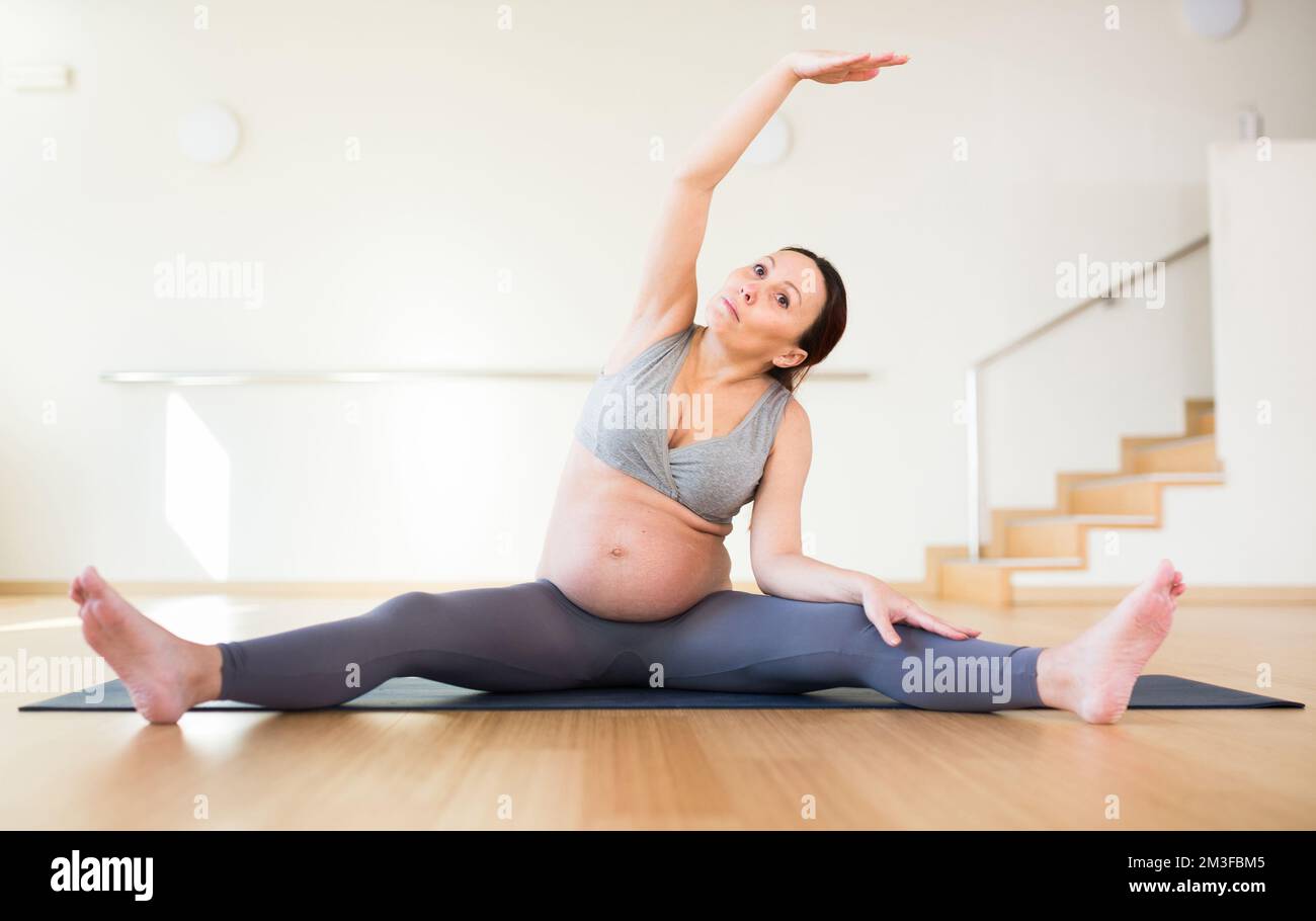 Pregnant woman is engaged in yoga. Revolved seated side angle pose or Parivrtta Upavistha Konasana Stock Photo