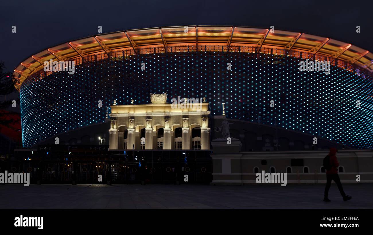 A huge illuminated stadium at night. Stock footage.A tall large stadium fenced with a fence illuminated by different lights and next to which people w Stock Photo