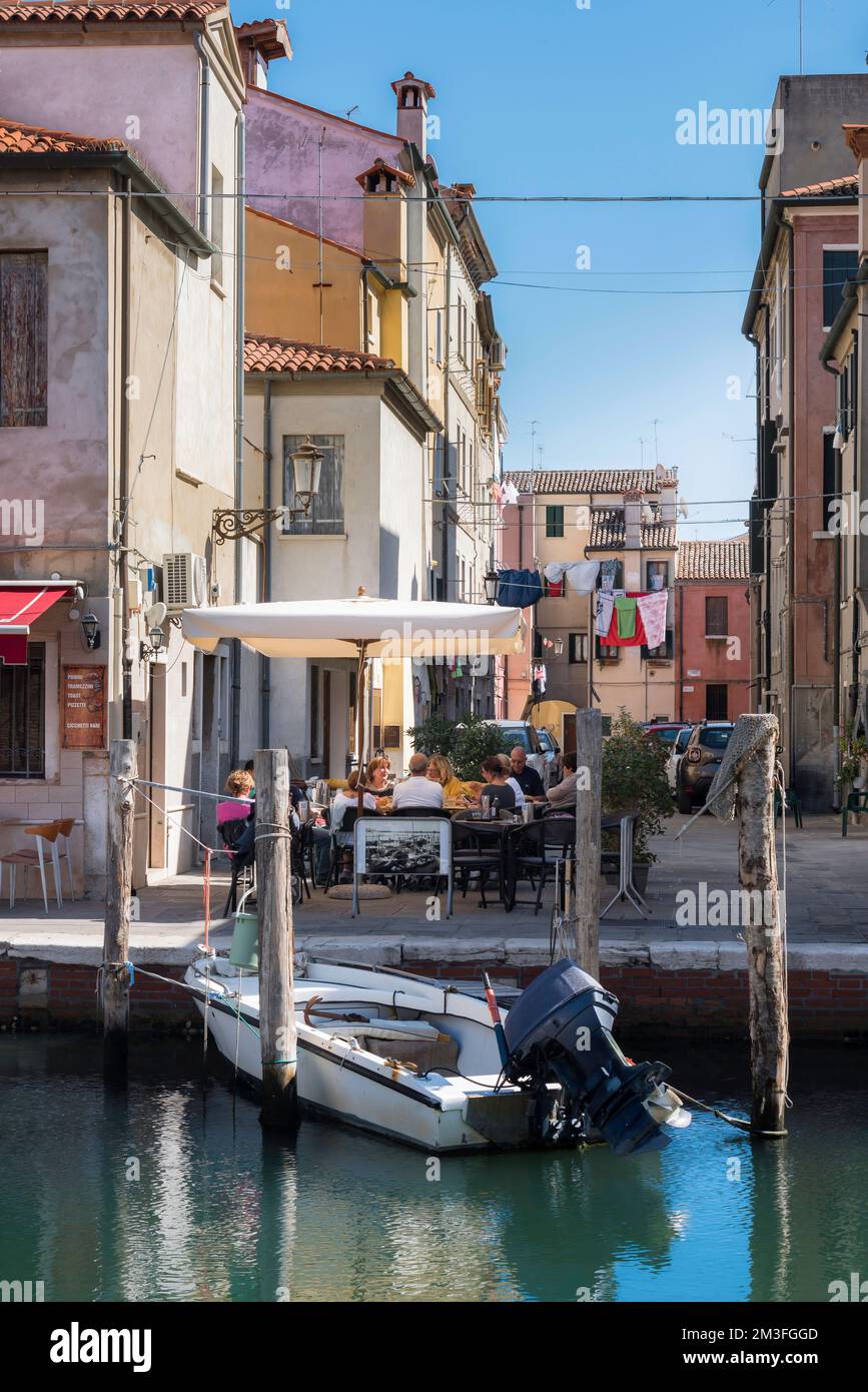 Canal Italy restaurant, view in summer of a group of people dining at a restaurant terrace beside the Canal Vena in Chioggia, Comune of Venice, Italy Stock Photo