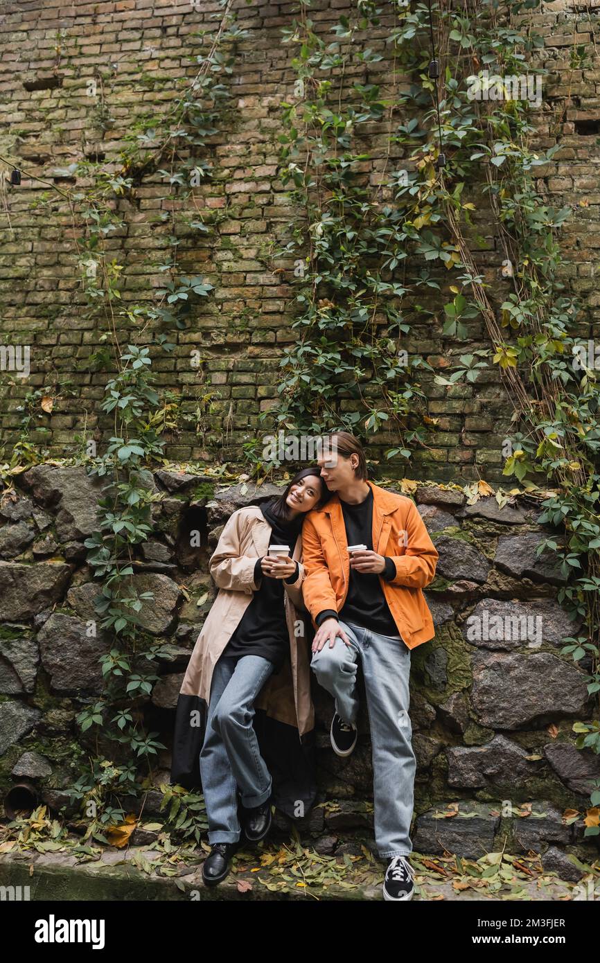 Smiling asian woman in trench coat looking at camera near boyfriend ...