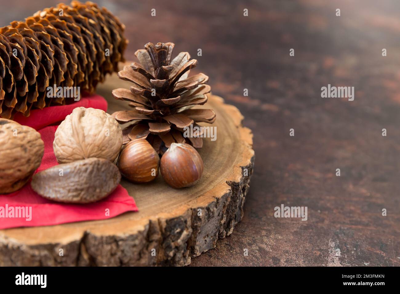 Festive still life with space for copy Christmas holidays post containing nuts and pinecones on a wooden block with red napkin and dark background. Stock Photo