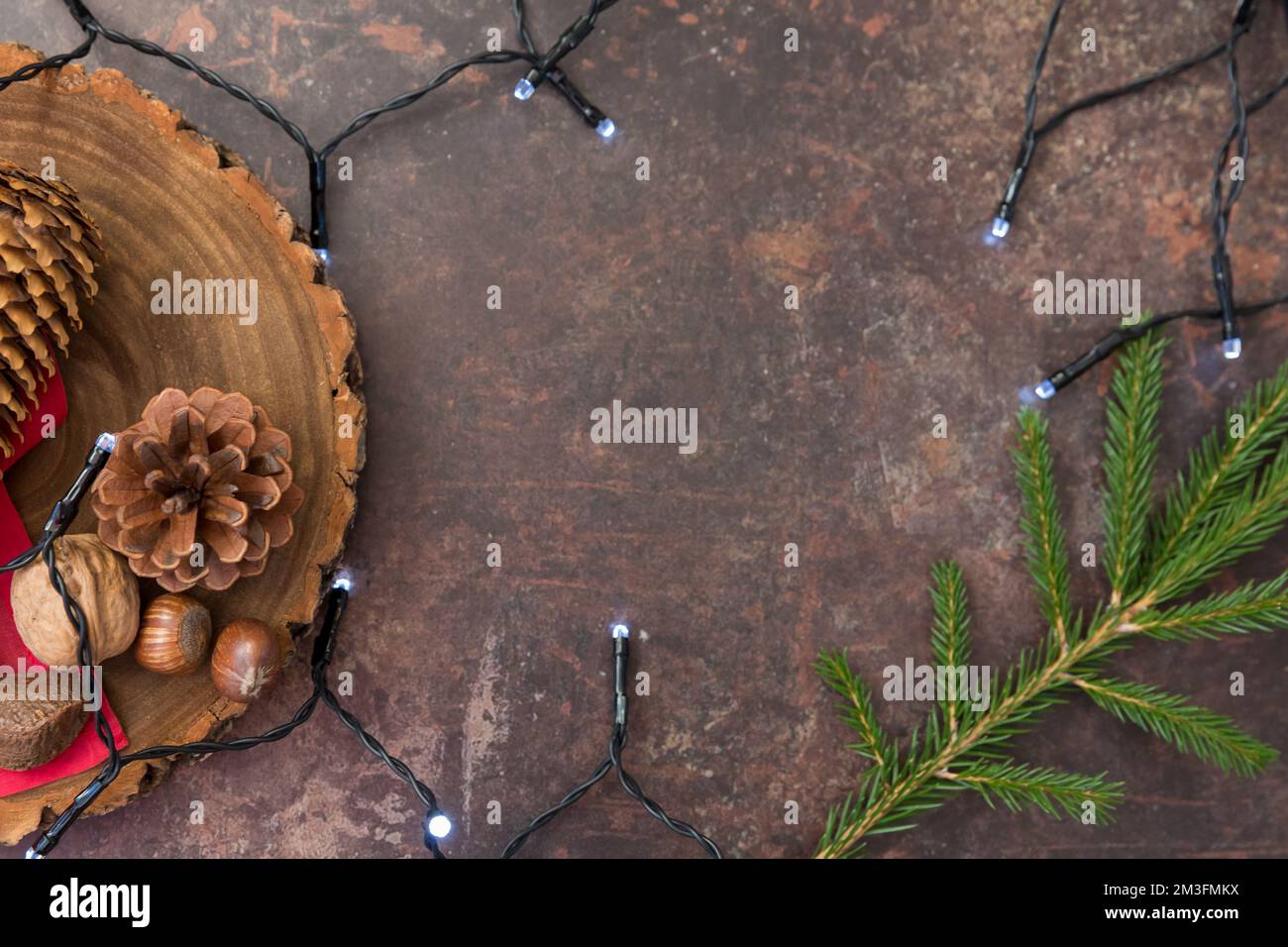 Christmas flatlay containing cones, nuts and fairy lights with space for copy against a dark background Stock Photo