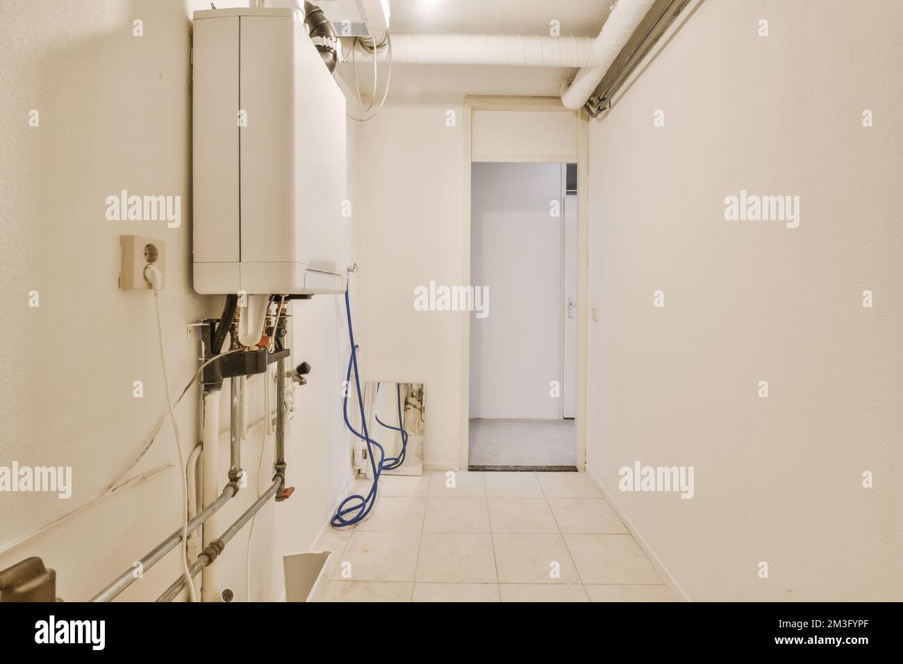 a very clean white room with some pipes and water heaters on the wall in this photo is taken from inside Stock Photo