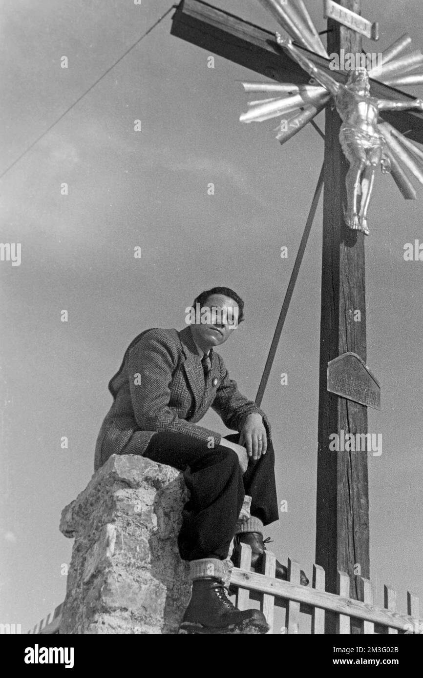 Auf dem Wankgipfel nach der Olympiade 1936 - Herrenportrait unter dem Gipfelkreuz auf dem Wank, Garmisch-Partenkirchen, 1936. On the Wank peak after the 1936 Olympics - Portrait of a man under the summit cross of Wank mountain, Garmisch-Partenkirchen, 1936. Stock Photo