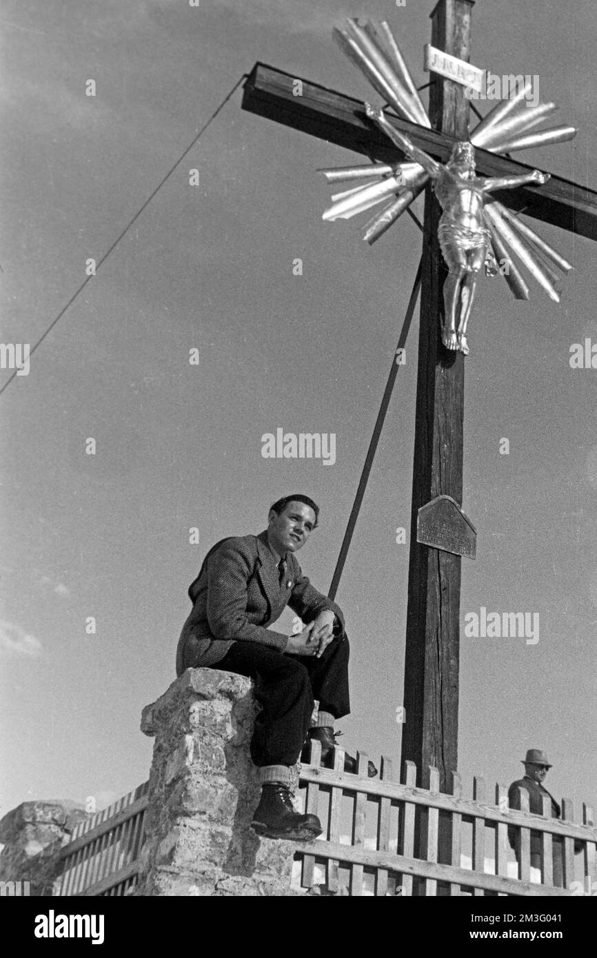 Auf dem Wankgipfel nach der Olympiade 1936 - Herrenportrait unter dem Gipfelkreuz auf dem Wank, Garmisch-Partenkirchen, 1936. On the Wank peak after the 1936 Olympics - Portrait of a man under the summit cross of Wank mountain, Garmisch-Partenkirchen, 1936. Stock Photo