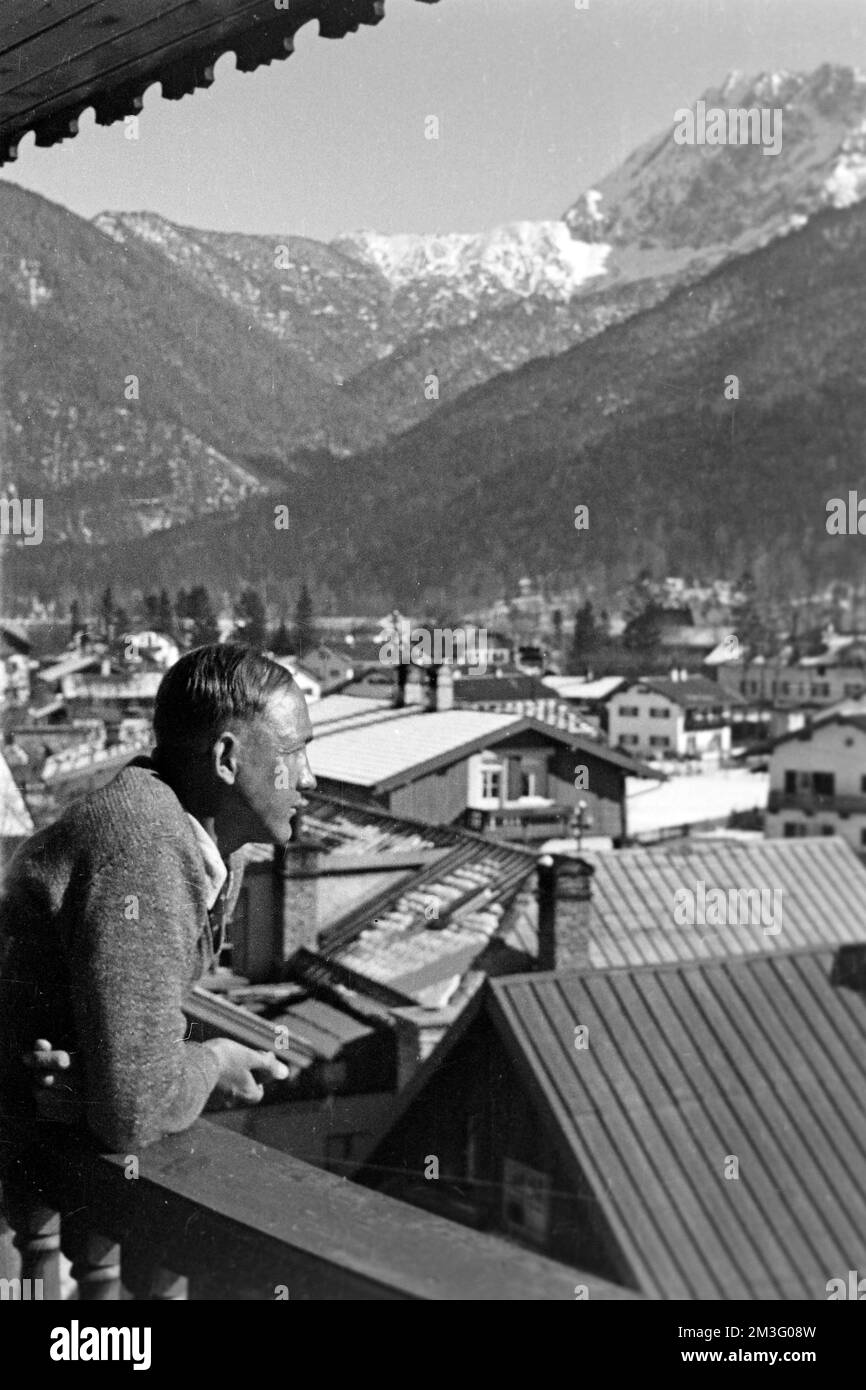 Mann blickt vom Balkon in Garmisch-Partenkirchen, 1936. Man gazing over the balcony's railing in Garmisch-Partenkirchen, 1936. Stock Photo