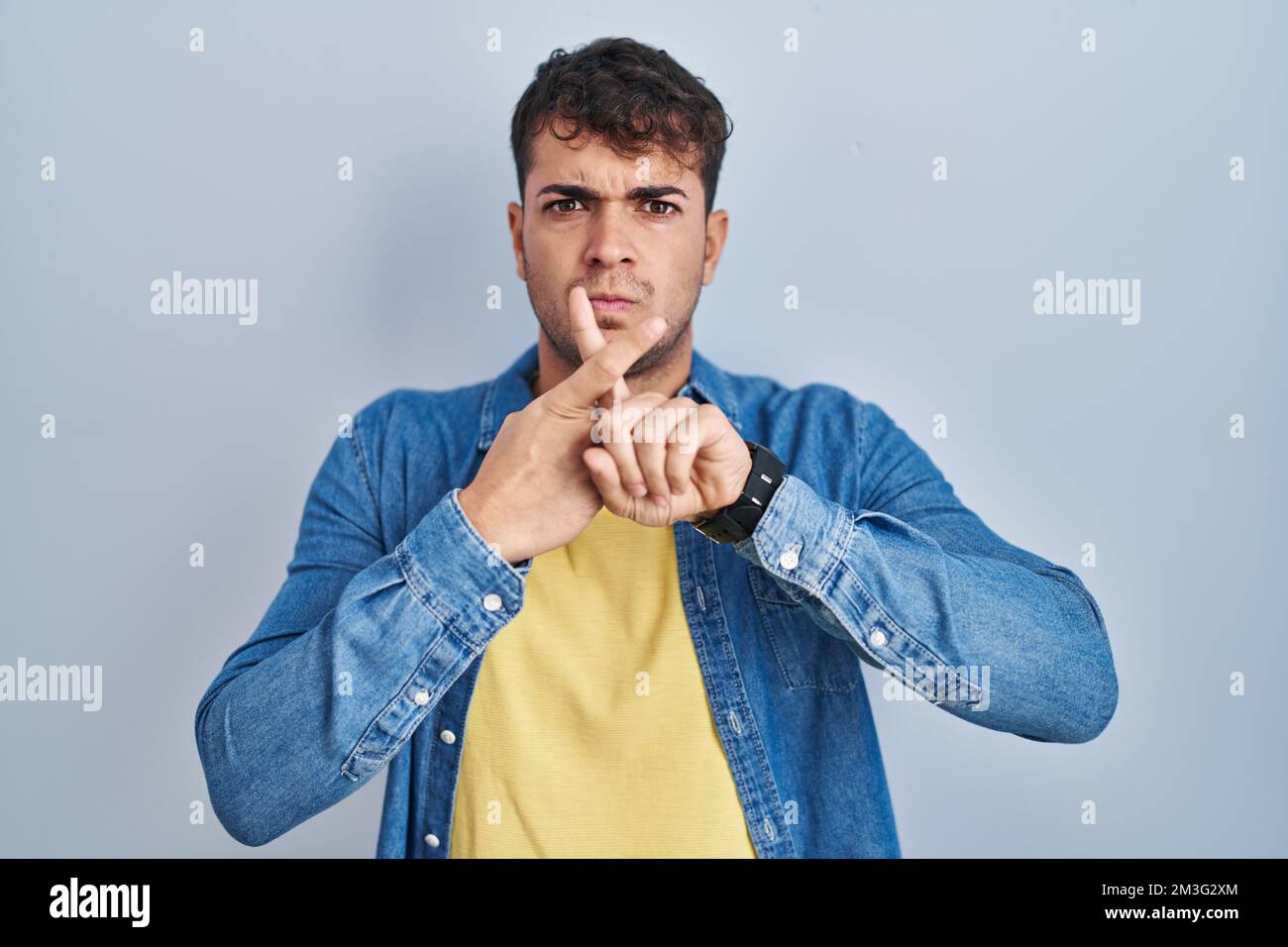Young hispanic man standing over blue background rejection expression ...