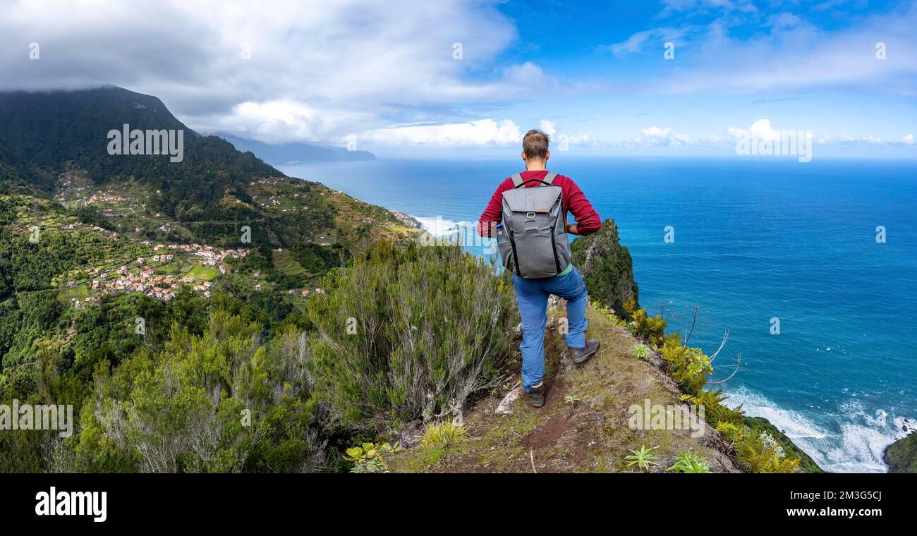 Hikers on the ridge of Pico do Alto, view of densely overgrown mountains and village of Boaventura, view of coast and sea, Madeira, Portugal Stock Photo