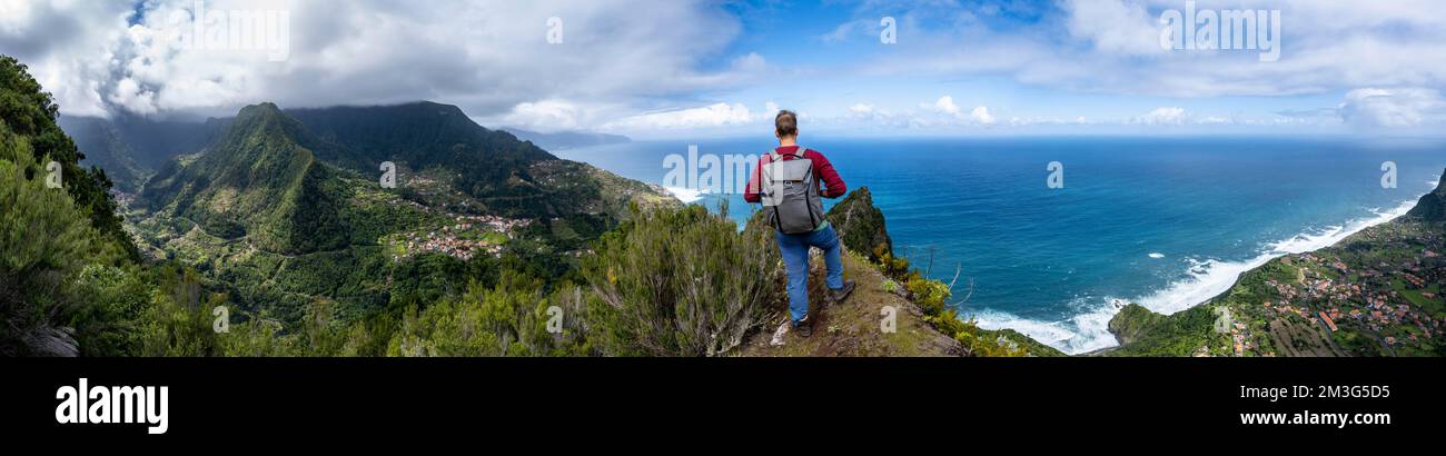Hikers on the ridge of Pico do Alto, panorama, view of densely overgrown mountains and the village of Boaventura, view of the coast and sea with the Stock Photo