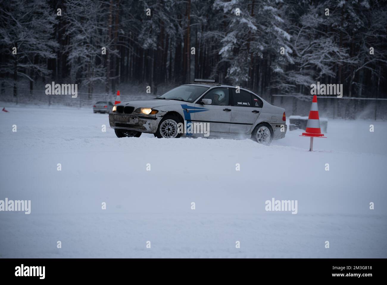 12-12-2022 Riga, Latvia  a car driving through a snow covered forest area with a red and white traffic cone in the foreground. . Stock Photo