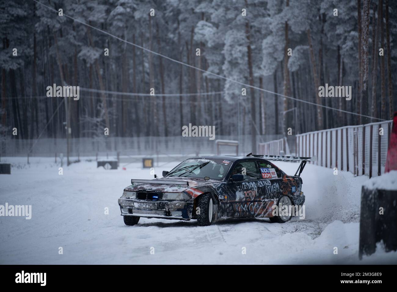 12-12-2022 Riga, Latvia  a car that is parked in the snow near a fence and trees in the background. . Stock Photo