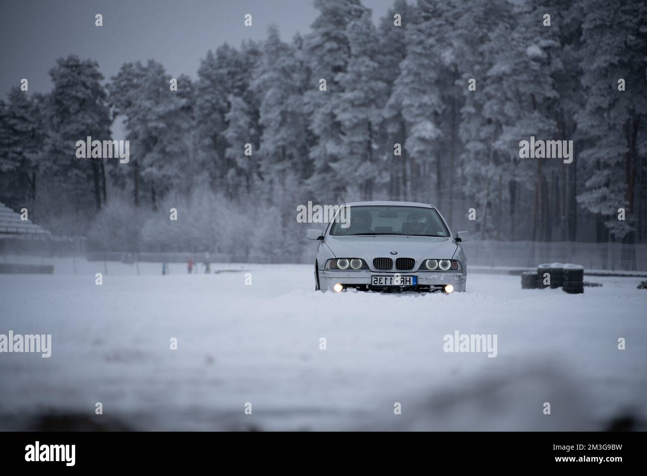 12-12-2022 Riga, Latvia  a car is parked in the snow near a forest of trees and a building with a snow covered roof. . Stock Photo