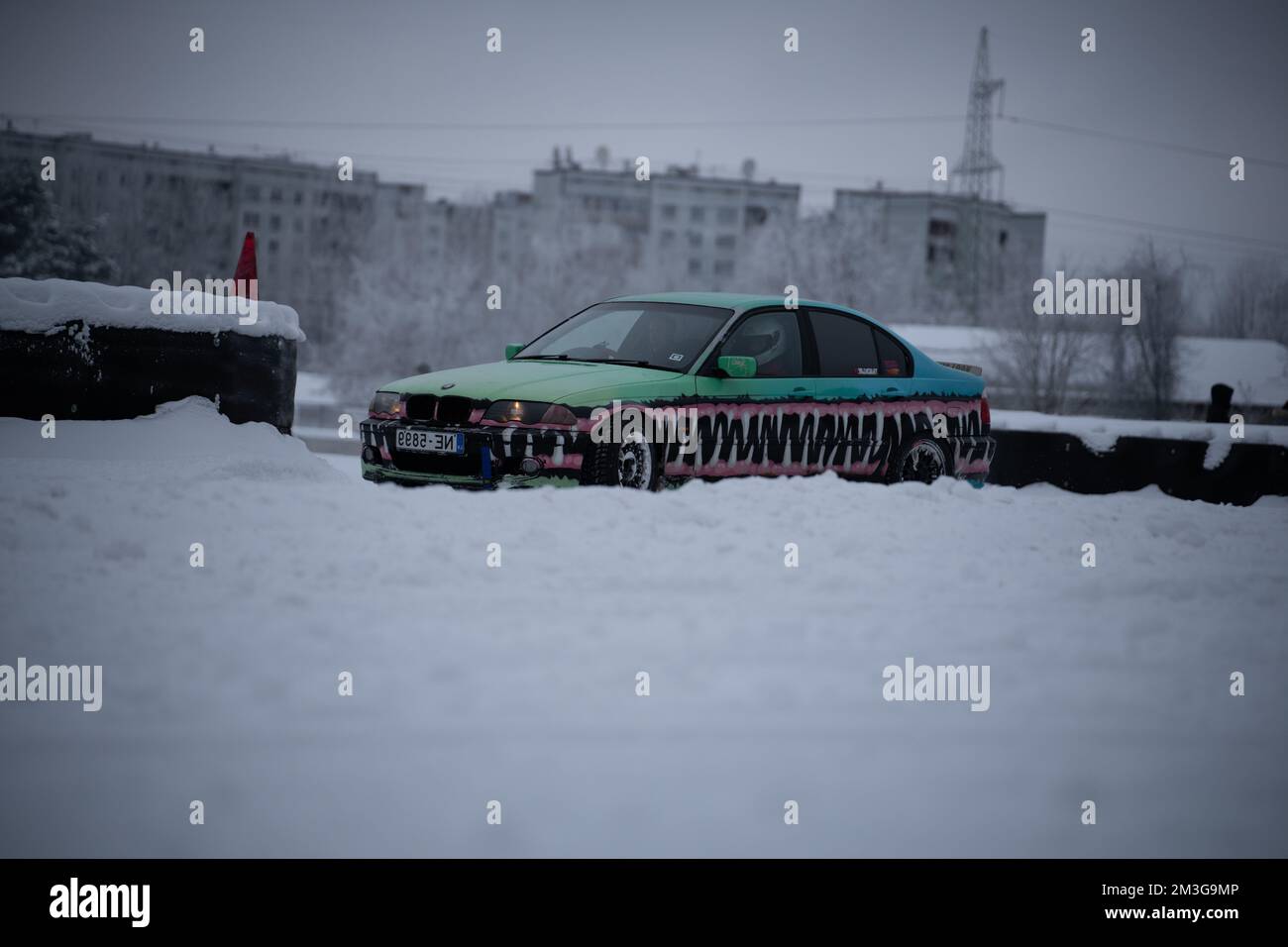 12-12-2022 Riga, Latvia  a car parked in the snow with a snowboard on it's hood and a building in the background. . Stock Photo