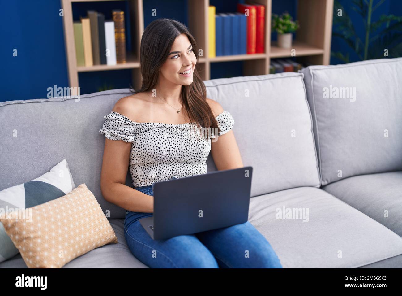 Young beautiful hispanic woman using laptop sitting on sofa at home ...