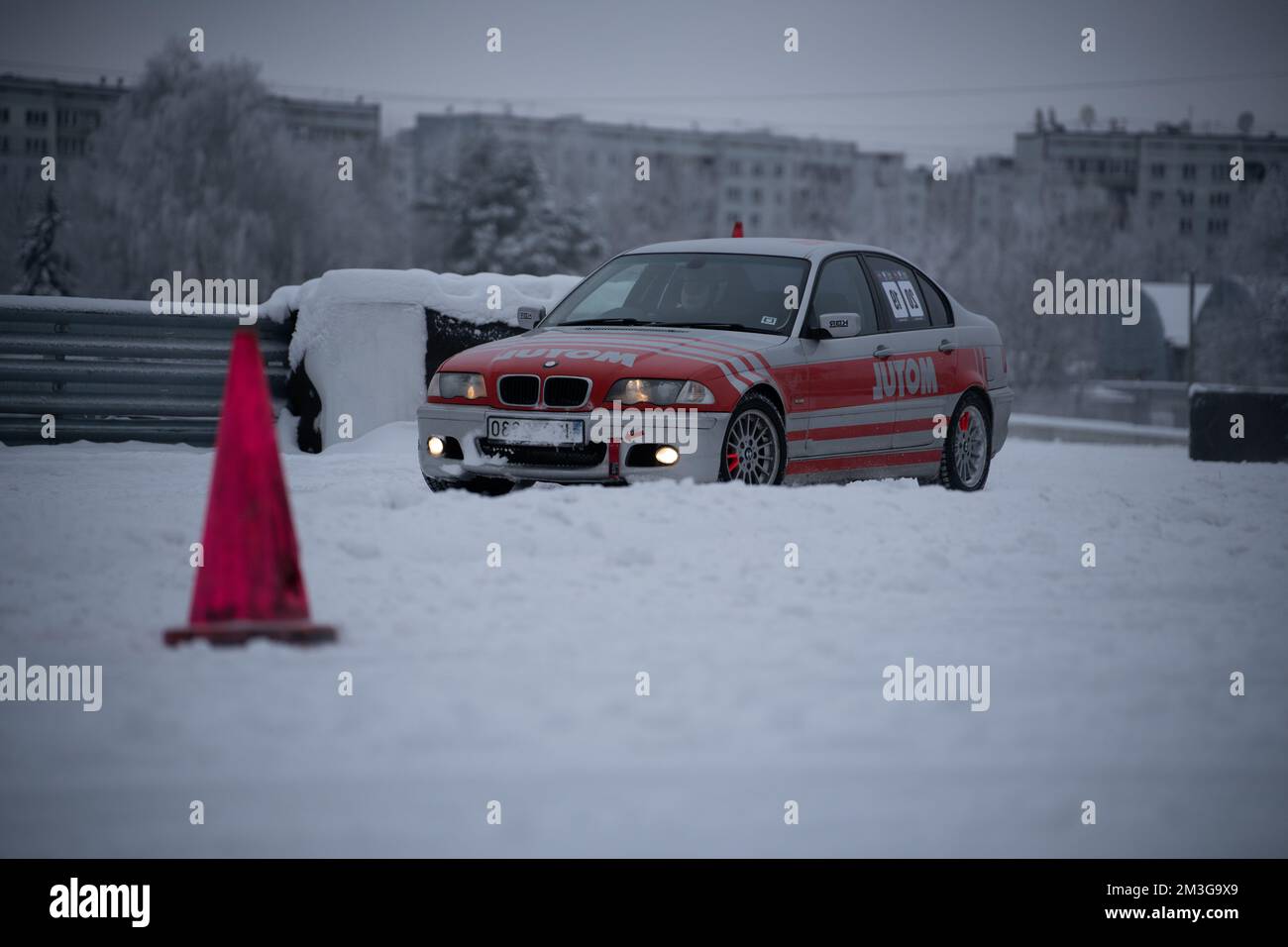 12-12-2022 Riga, Latvia  a red car parked in the snow next to a red cone and a red traffic cone on a street. . Stock Photo