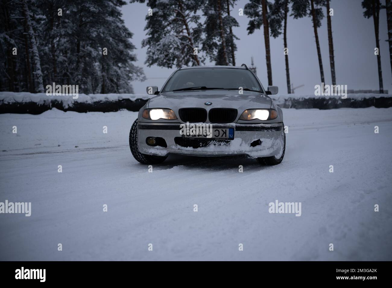 12-12-2022 Riga, Latvia  a white car driving down a snow covered road next to trees and a forest in the background with a few snow on the ground. . Stock Photo