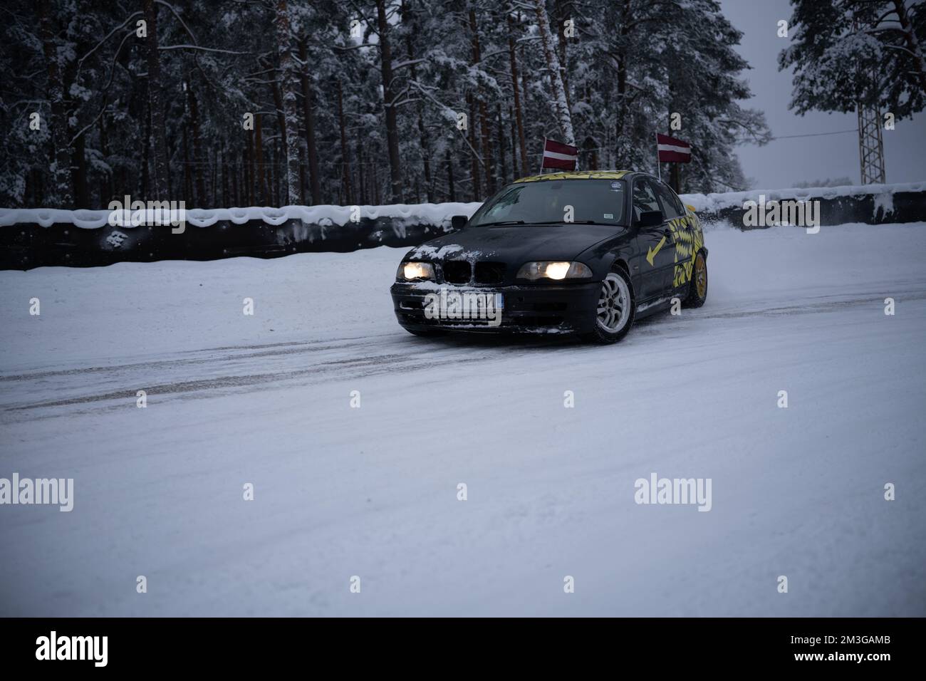 12-12-2022 Riga, Latvia  a car driving down a snowy road in the snow with trees in the background and a flag on top of the car. . Stock Photo