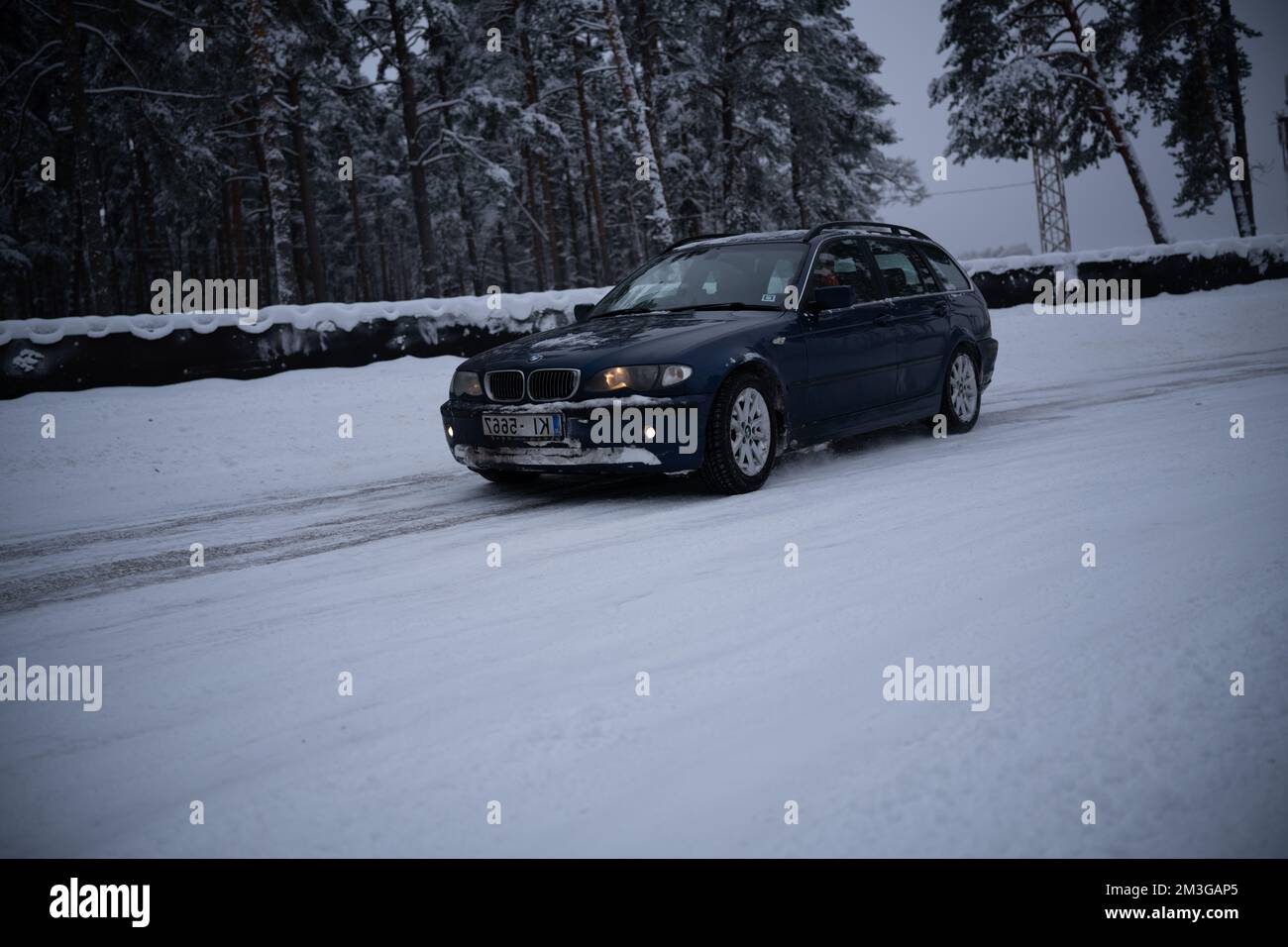 12-12-2022 Riga, Latvia  a car driving down a snowy road in the snow with trees in the background and a fence in the foreground. . Stock Photo