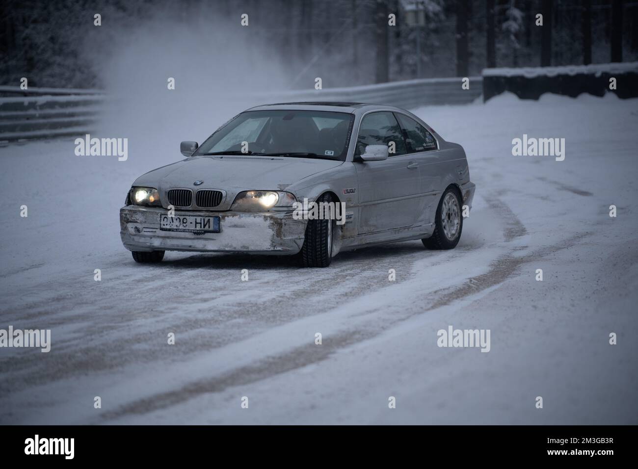12-12-2022 Riga, Latvia  a white car driving down a snow covered road in the snow with headlights on it's headlight. . Stock Photo