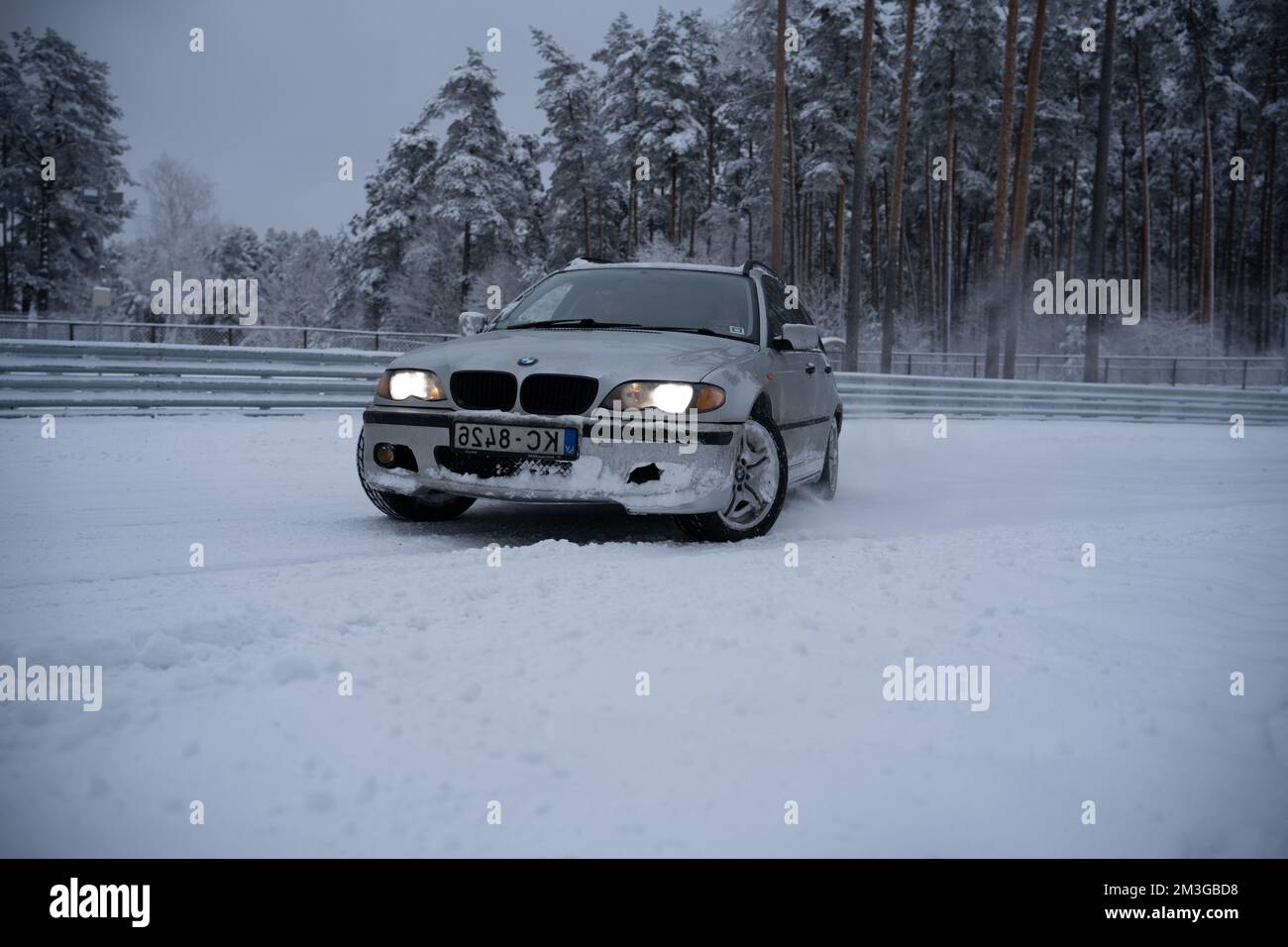 12-12-2022 Riga, Latvia  a car is driving through the snow in the woods on a road with trees in the background and a fence in the foreground. . Stock Photo