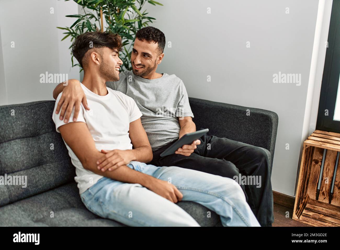 Two hispanic men couple using touchpad hugging each other at home Stock ...