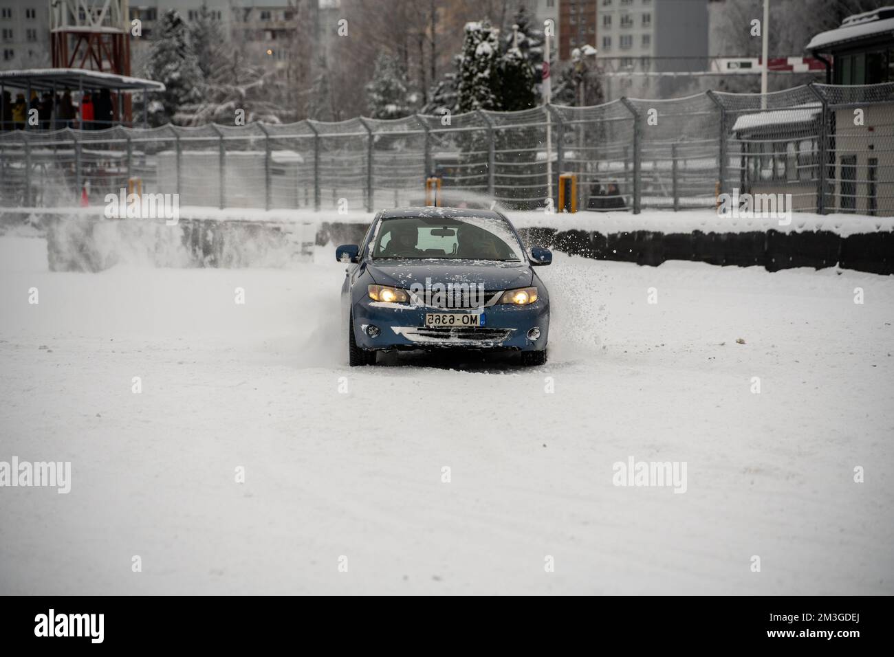 12-12-2022 Riga, Latvia  a car driving through a snow covered street next to a fence and a building with a clock on it. . Stock Photo