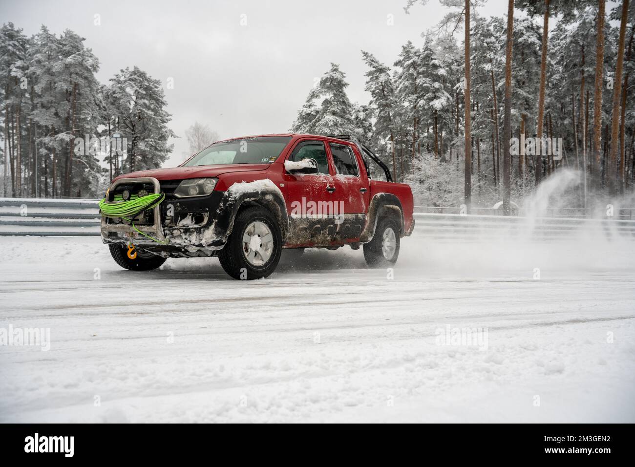 12-12-2022 Riga, Latvia  a red truck driving down a snow covered road next to a forest of trees and a fence with snow on it. . Stock Photo