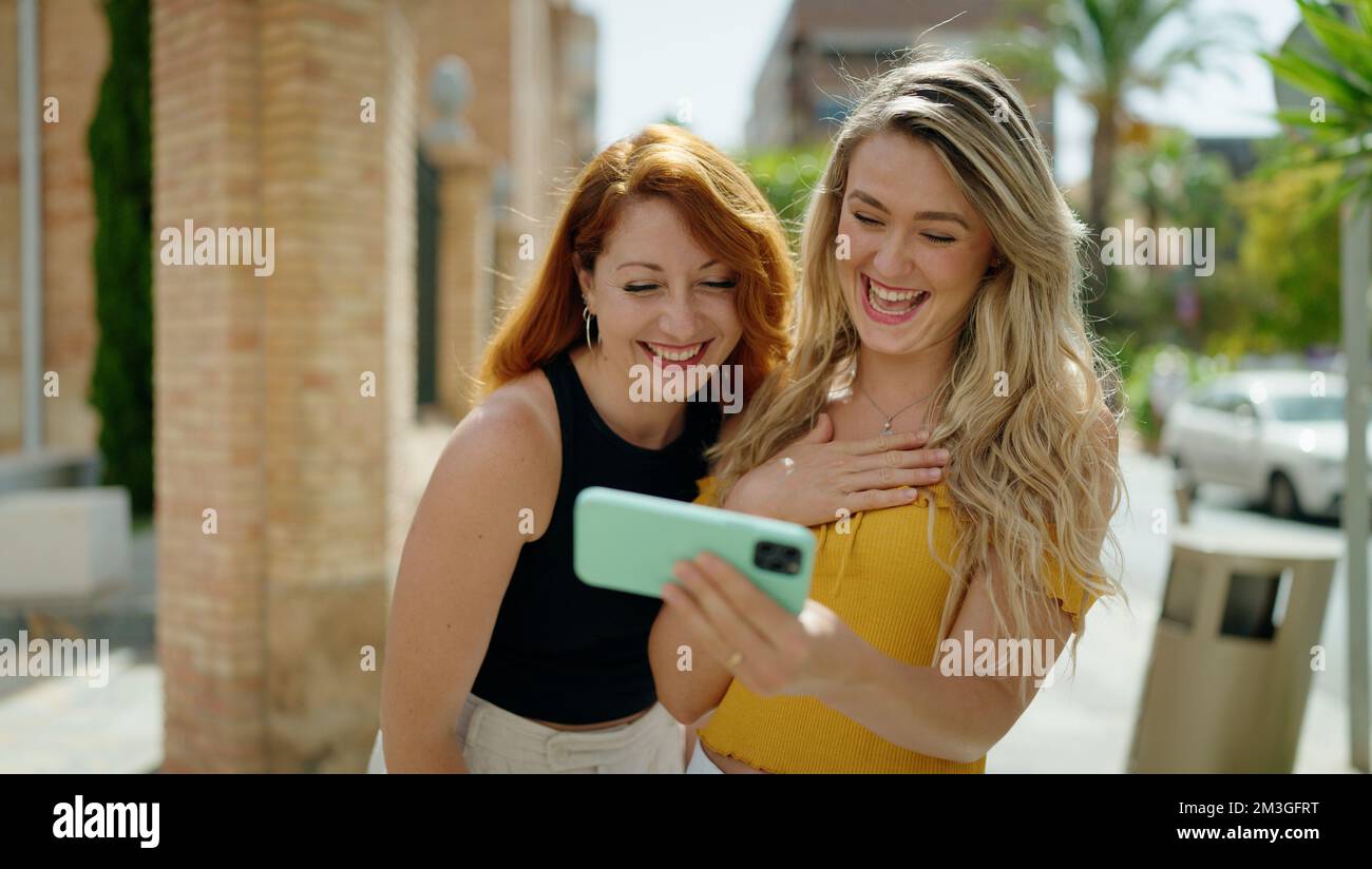 Two women standing together watching video on smartphone at street ...