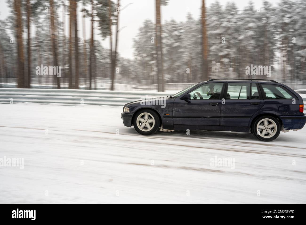 12-12-2022 Riga, Latvia  a black car driving down a snowy road next to a forest of trees and snow covered ground with no one in it. . Stock Photo