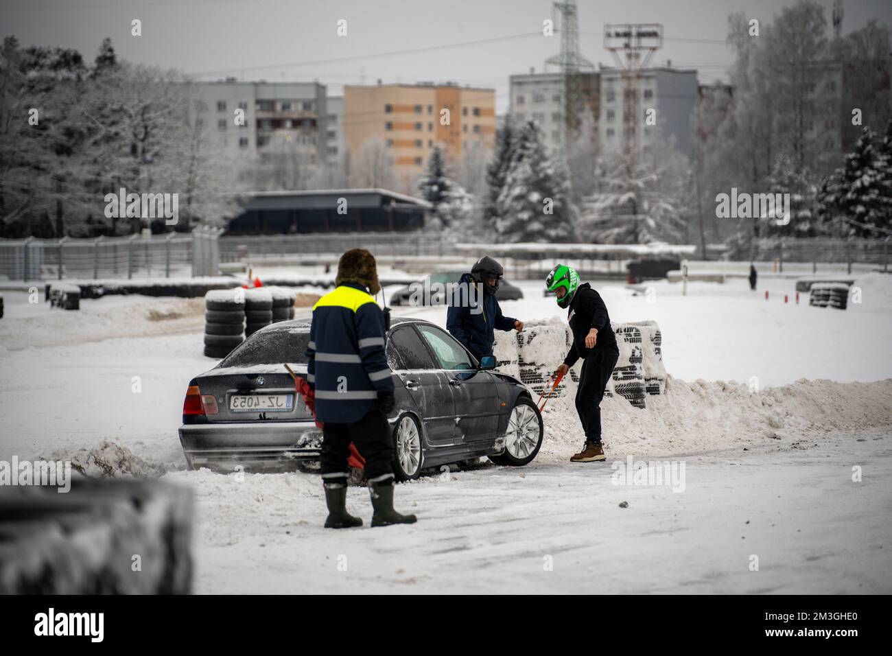 12-12-2022 Riga, Latvia  a group of people standing around a car in the snow with a snow blower on it's hood. . Stock Photo