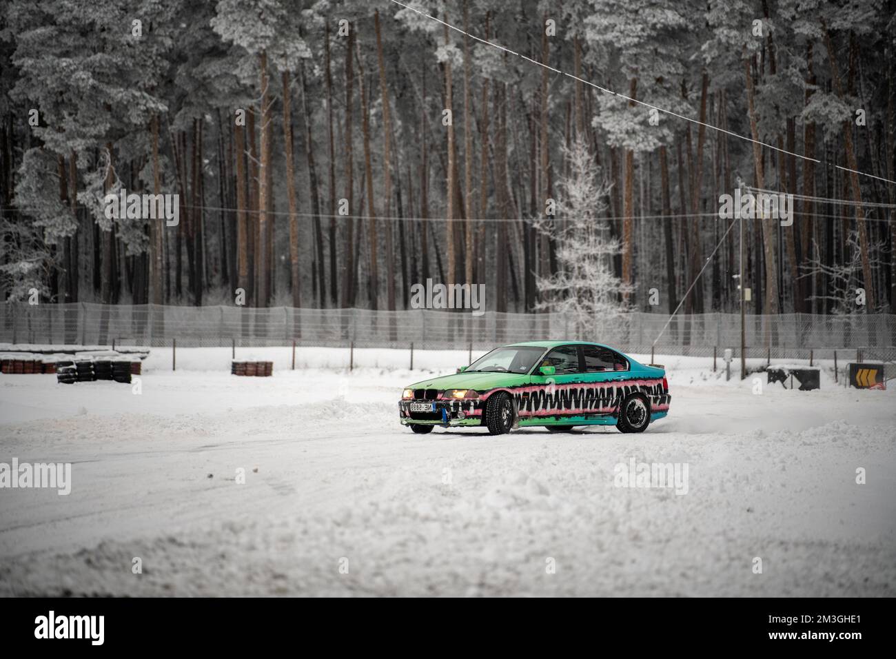 12-12-2022 Riga, Latvia  a car is parked in the snow near a forest with trees and a fence in the background. . Stock Photo