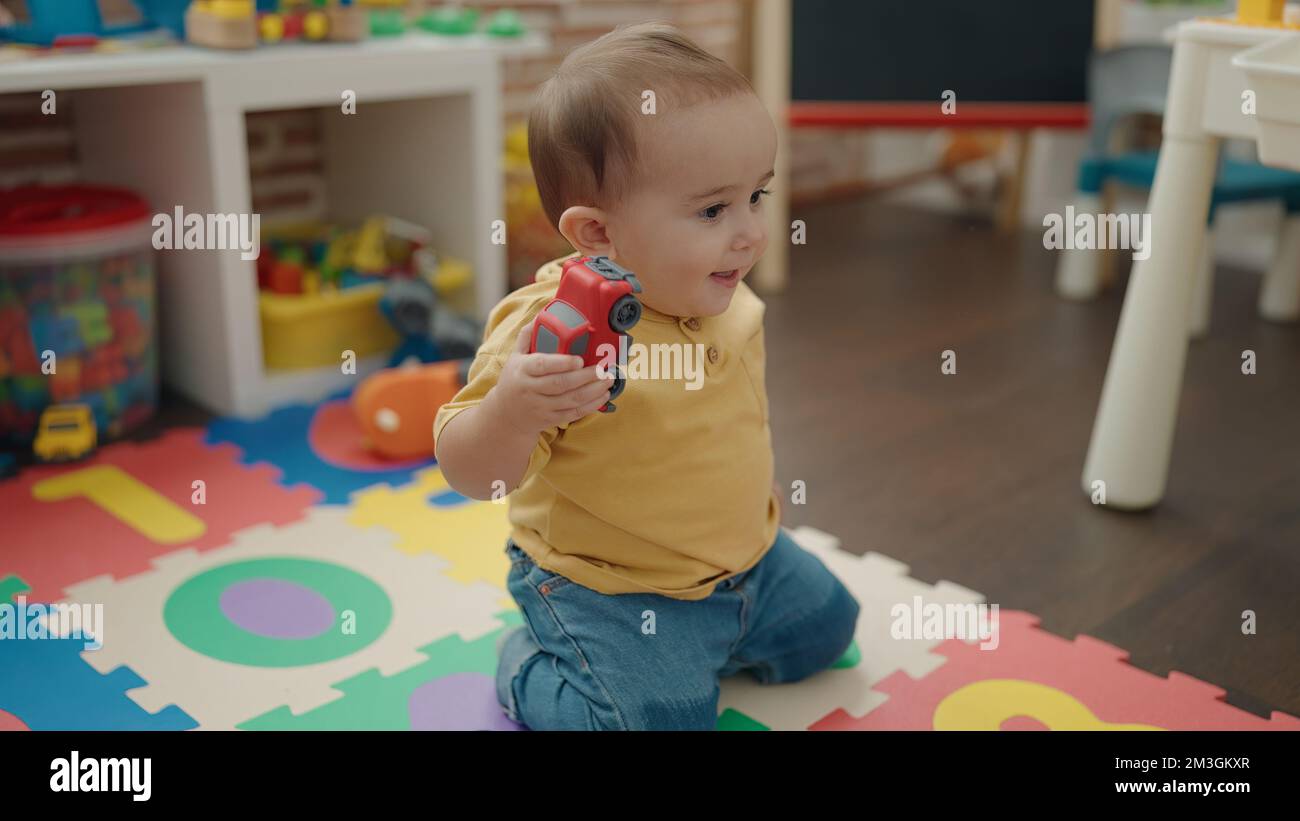 Adorable hispanic baby playing with car toy sitting on floor at ...