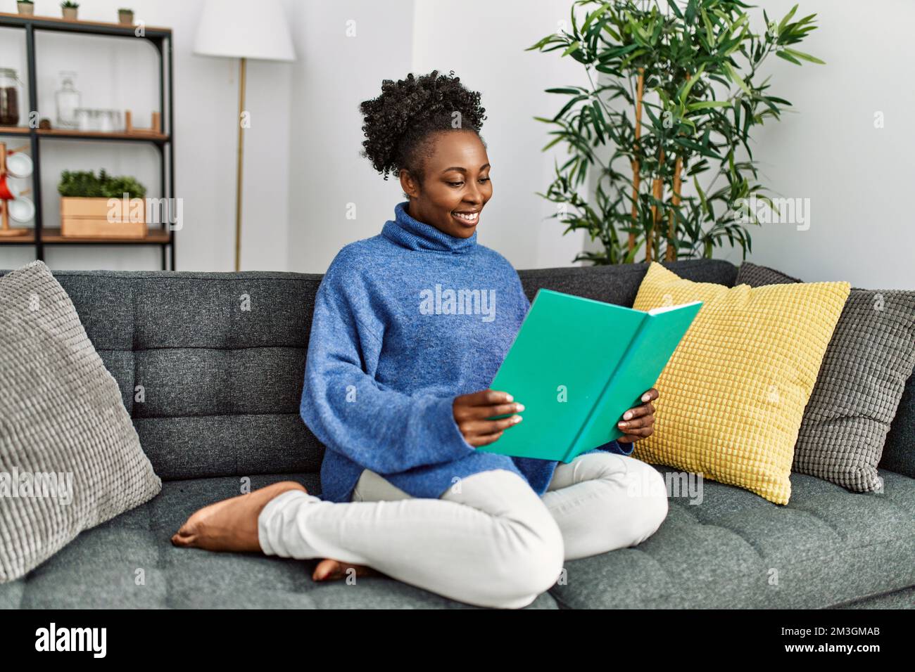 African american woman reading book sitting on sofa at home Stock Photo ...
