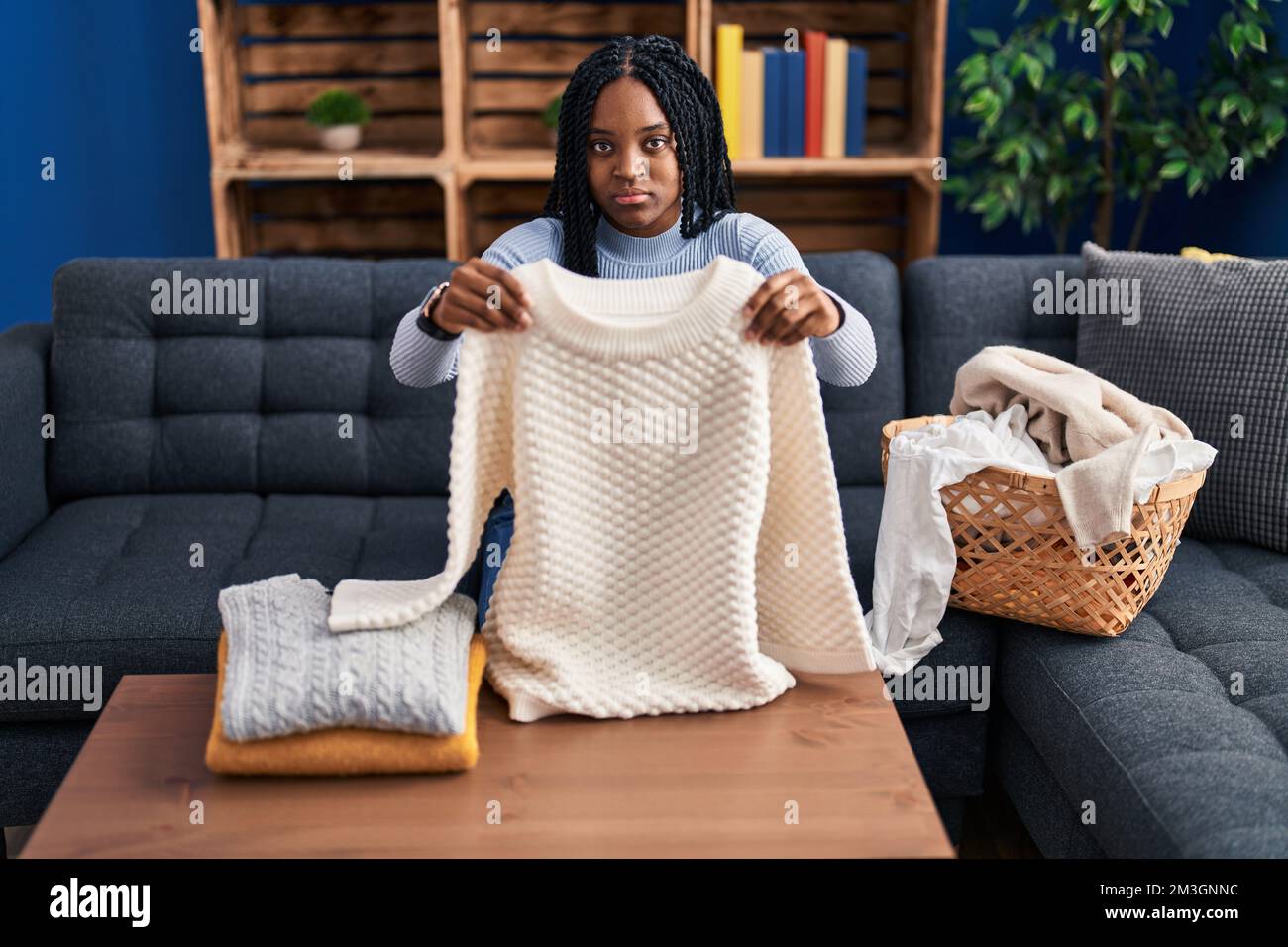 African american woman folding clean laundry skeptic and nervous