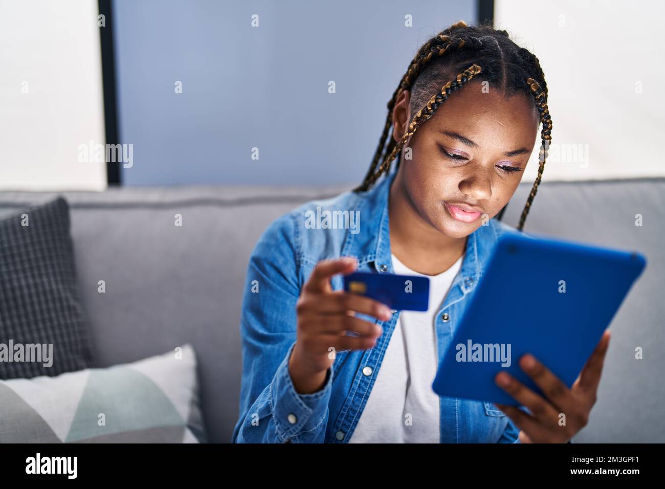 African american woman using touchpad and credit card sitting on sofa ...