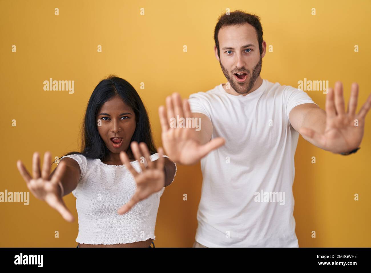 Interracial couple standing over yellow background doing stop gesture with hands palms, angry and frustration expression Stock Photo