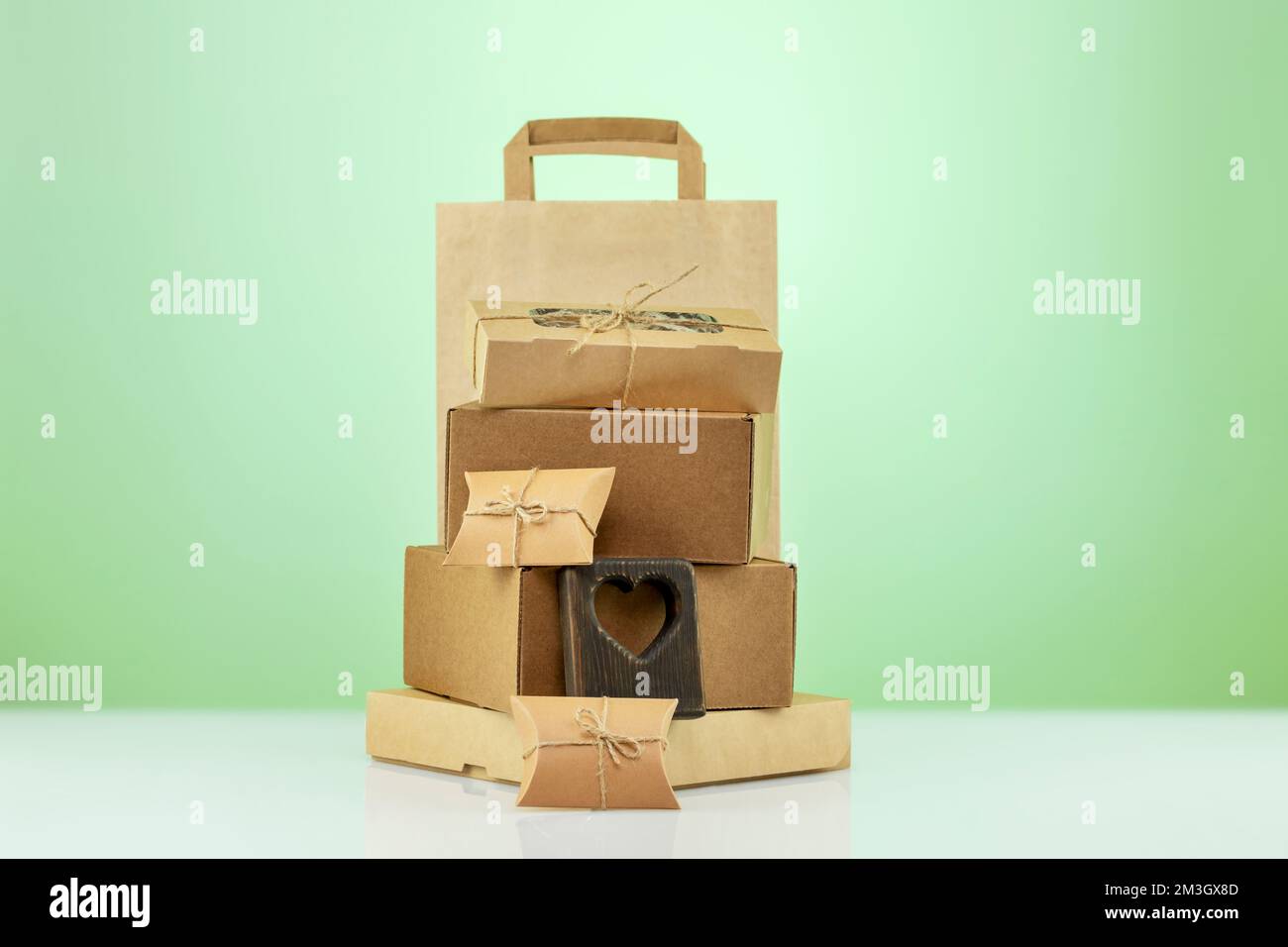 Eco friendly shopping and delivery service. Craft cardboard gift boxes, paper bag and wooden heart on green background. Zero Waste, plastic free, eco Stock Photo