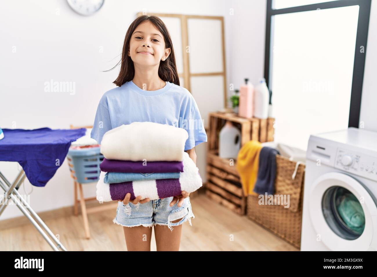 Young hispanic girl holding folded laundry smiling with a happy and ...
