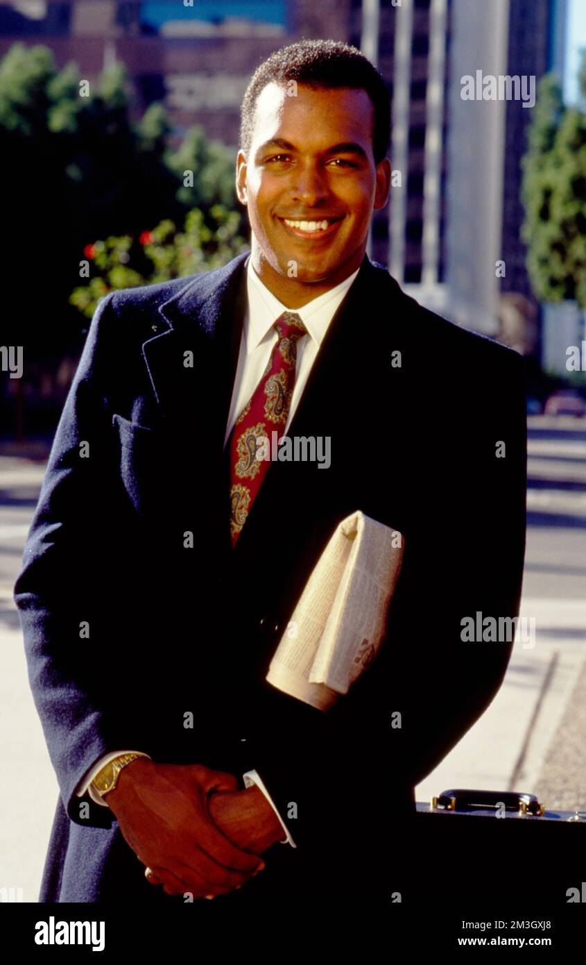 African-American businessman in suite posing with newspaper under his arm looking at the camera Stock Photo