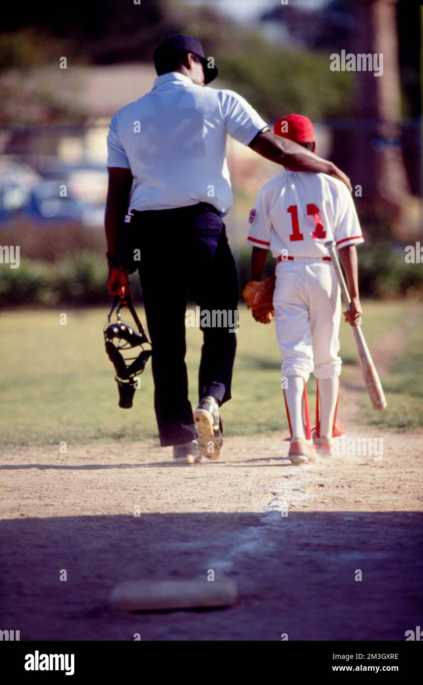 Baseball umpire walking off the field with his arm around child player Stock Photo