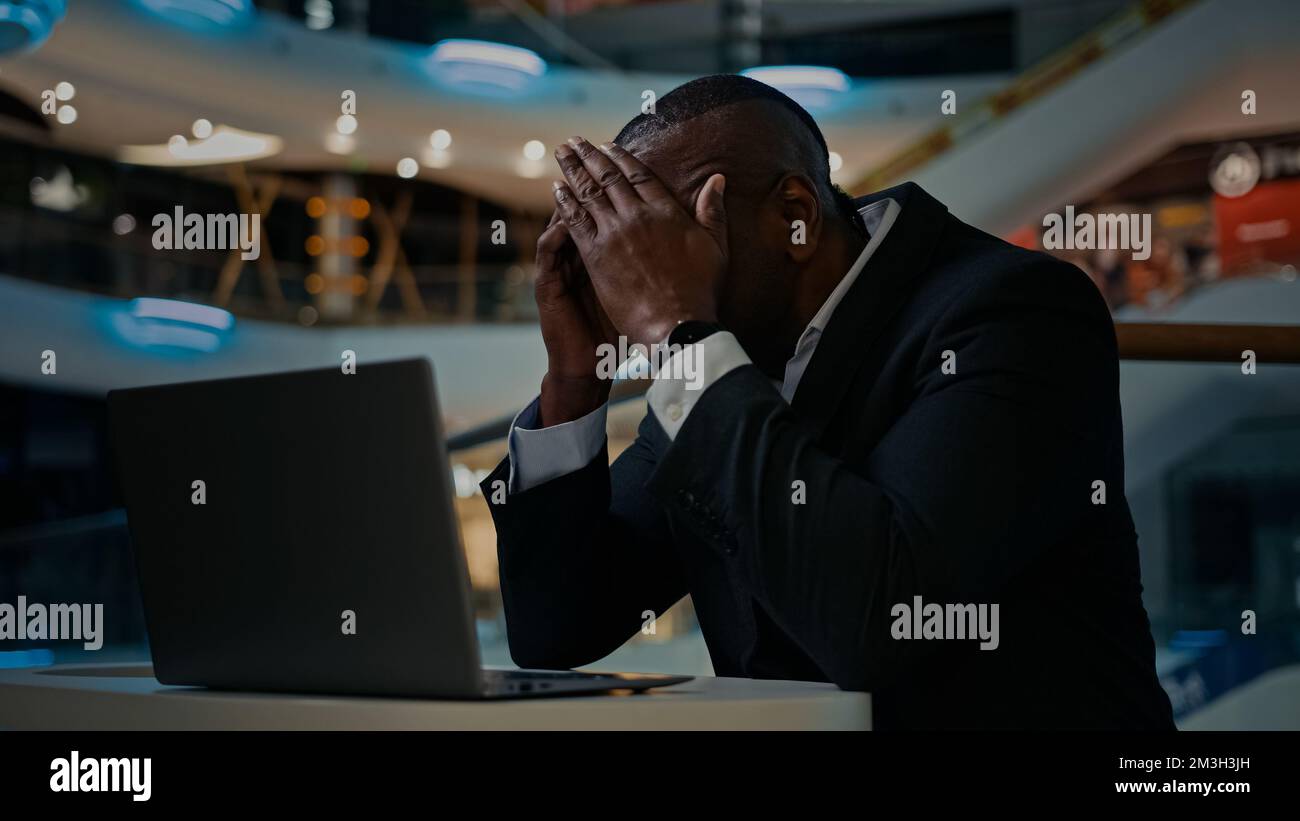 Middle-aged African businessman worker entrepreneur with laptop sad upset feel headache pain ache trouble with computer work adult man has problem Stock Photo