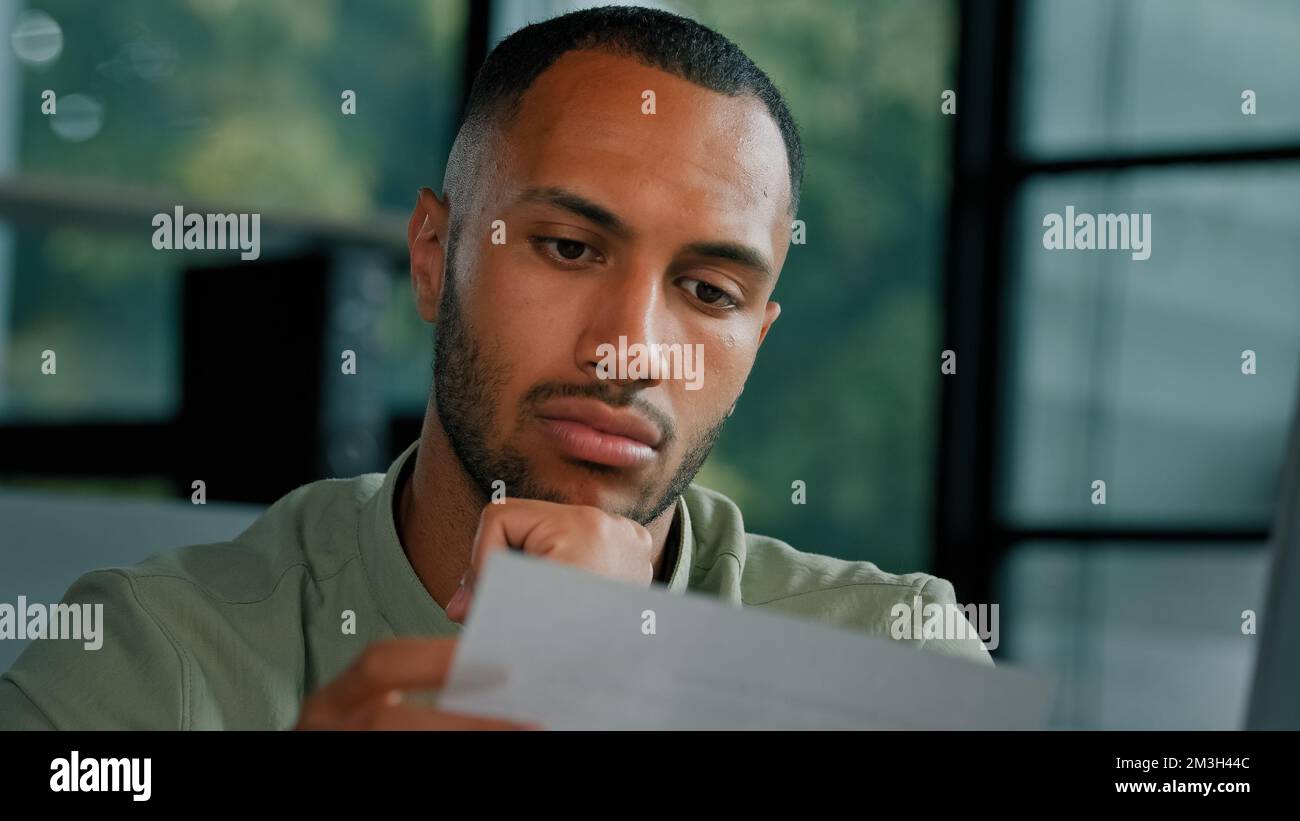 Calm African Latin guy man student entrepreneur open envelope notification from bank test result invitation reading news in paper admission letter at Stock Photo