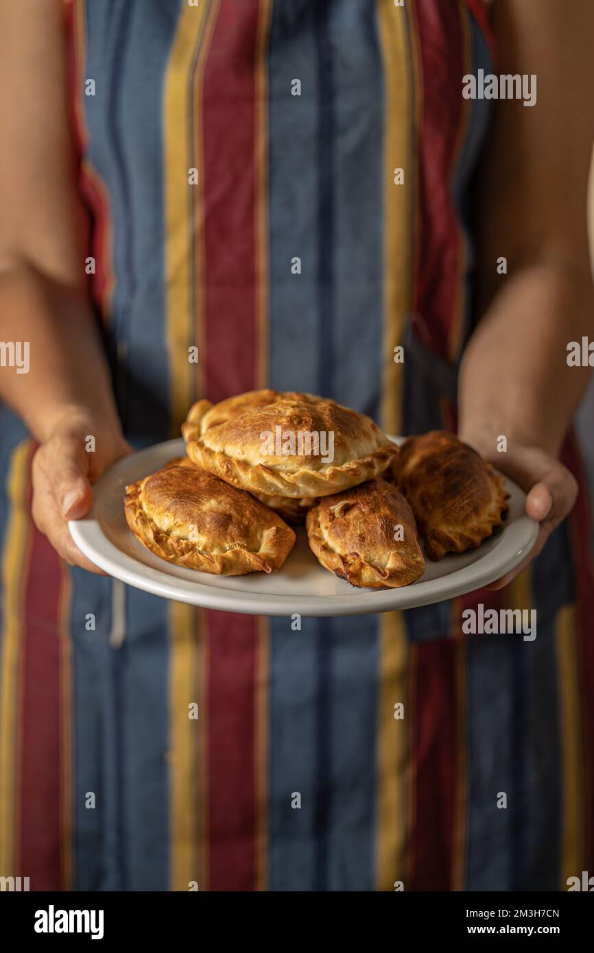 Woman in apron holding a tray with Argentine empanadas with copy space. Stock Photo