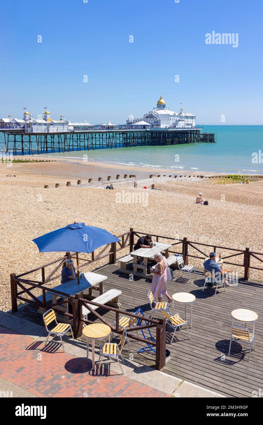 Eastbourne East Sussex Eastbourne pier Eastbourne beach and people sat at a promenade cafe on Eastbourne seafront Eastbourne England UK GB Europe Stock Photo