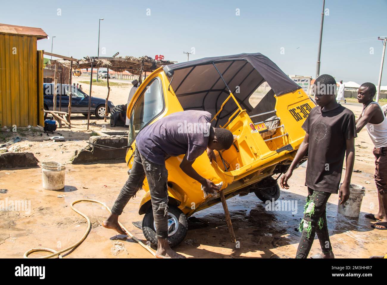 Car wash service in Africa, young boys working hard and cleaning local taxi (tuk-tuk) Stock Photo