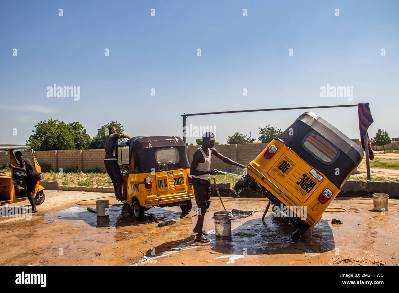 Car wash service in Africa, young boys working hard and cleaning local taxi (tuk-tuk) Stock Photo