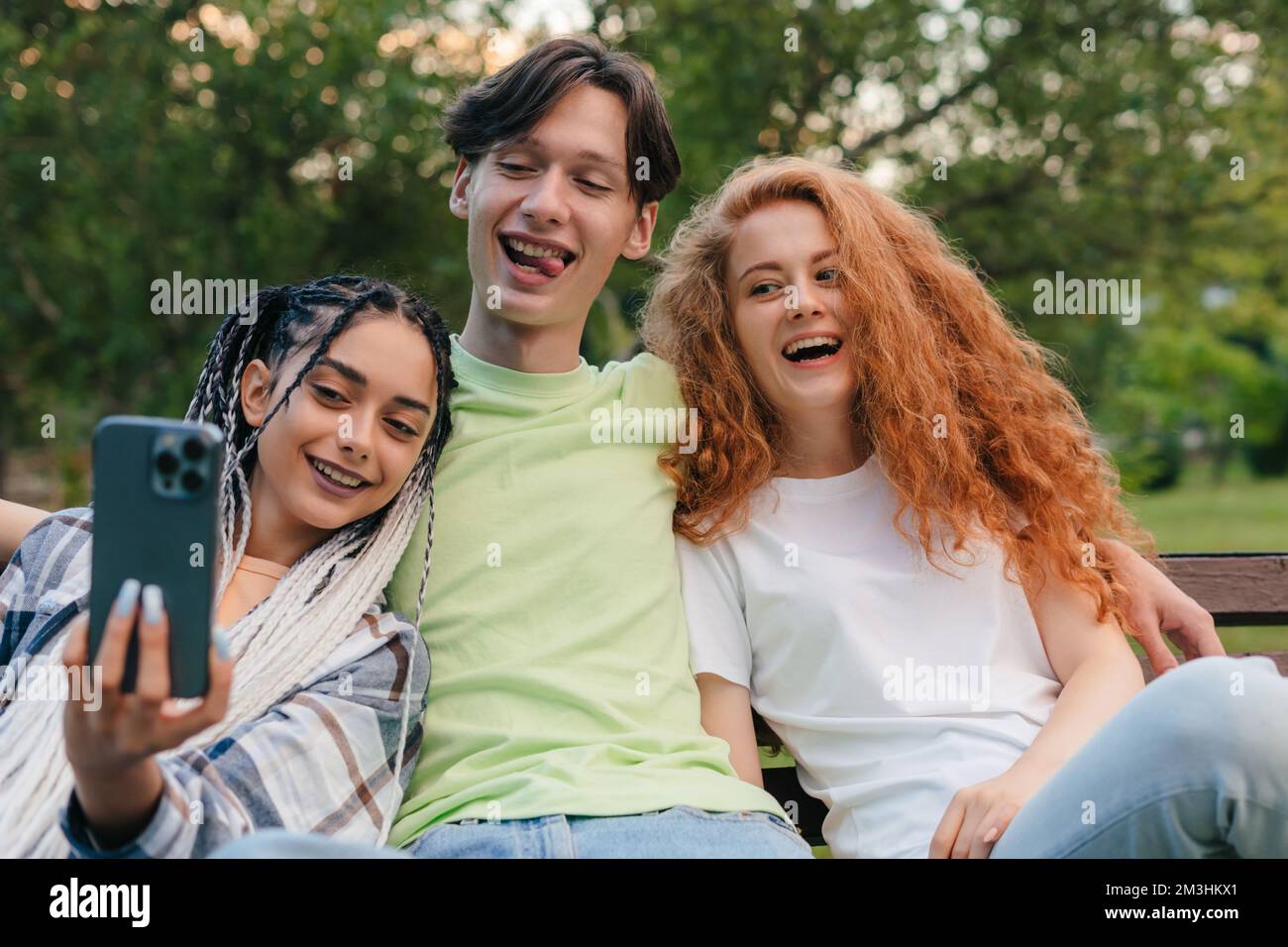 Cheerful smiling group of friends sitting on a bench in the city park ...