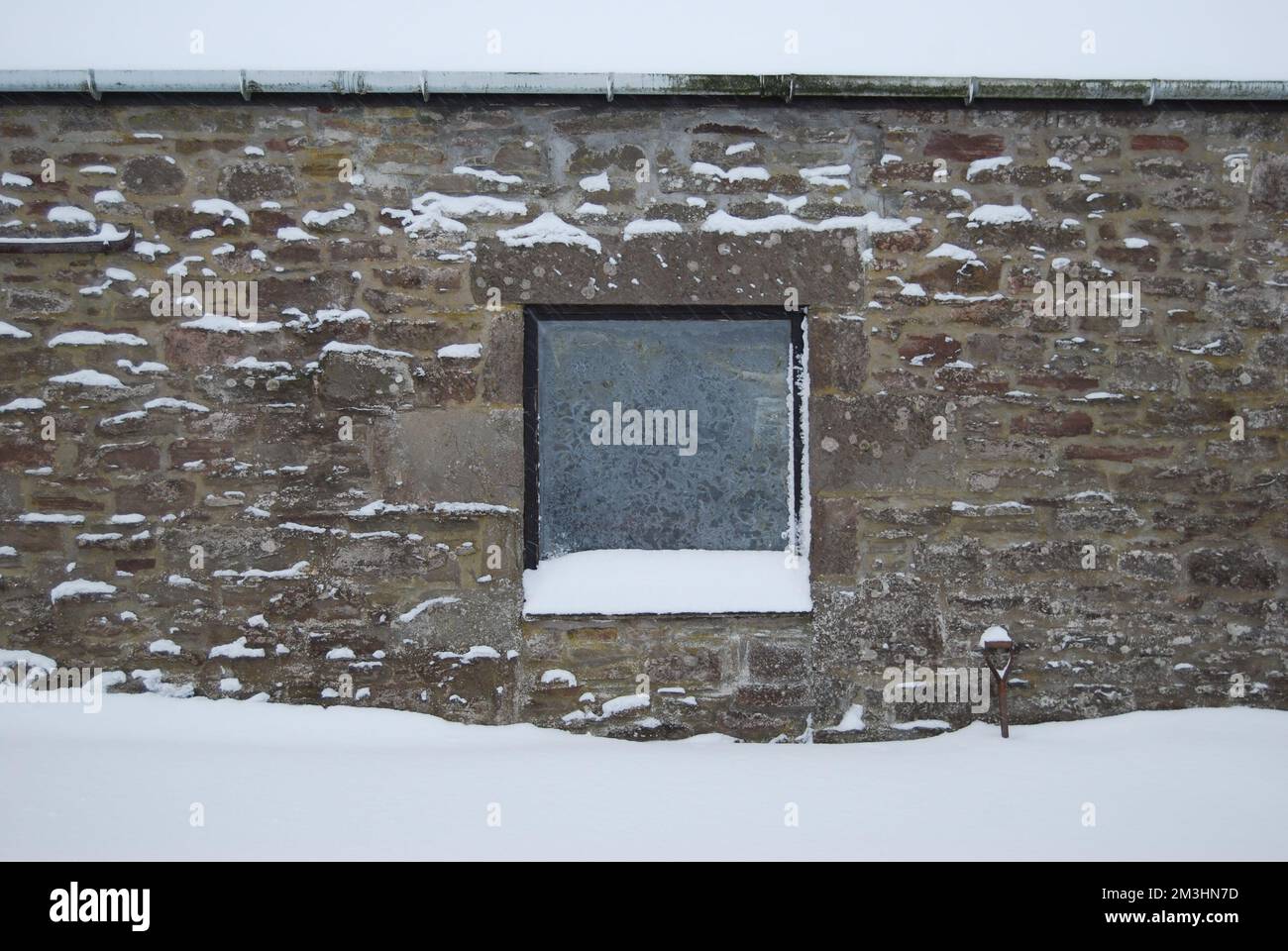 A snow drift against a stone wall with window, partly burying a spade. Stock Photo