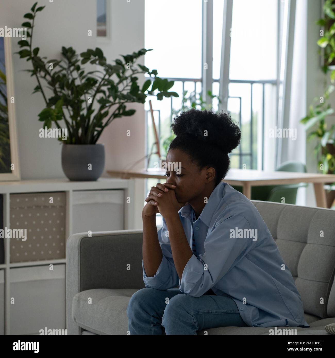 Oppressed African American woman with sad face sits on sofa thinking ...