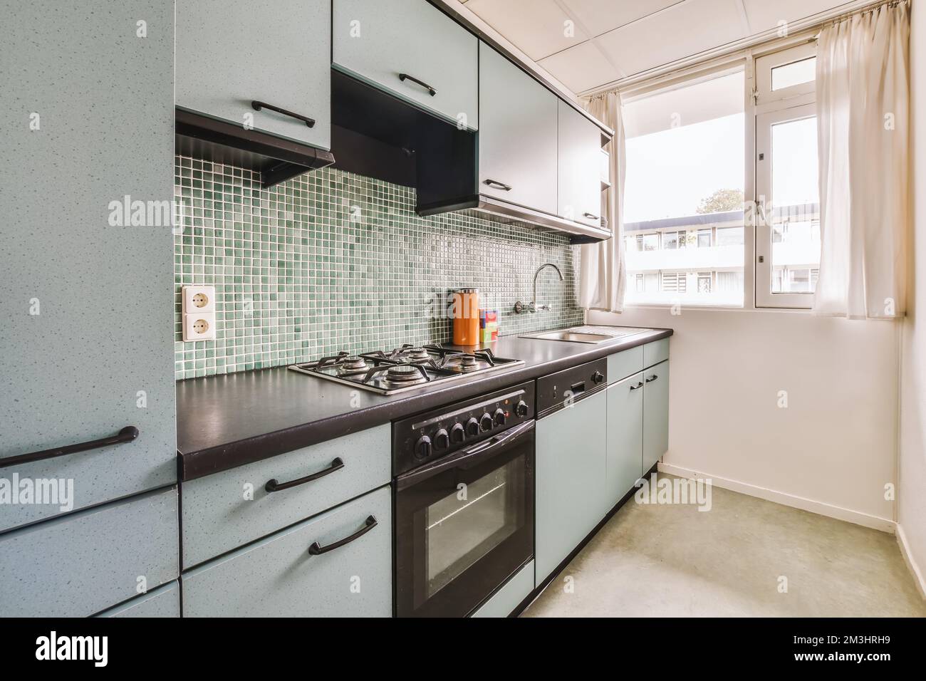 a kitchen with green tiles on the backs and white walls, including an oven in the sink is next to the stove Stock Photo